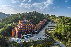 Un hotel con un edificio largo de color naranja, un estacionamiento y montañas al fondo.