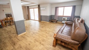 Une pièce spacieuse avec un plancher en bois, un canapé en cuir marron, un coin repas avec des chaises et une fenêtre avec des rideaux.