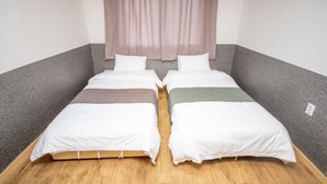 Une chambre double avec deux lits simples, une fenêtre avec des rideaux légers et un plancher en bois.