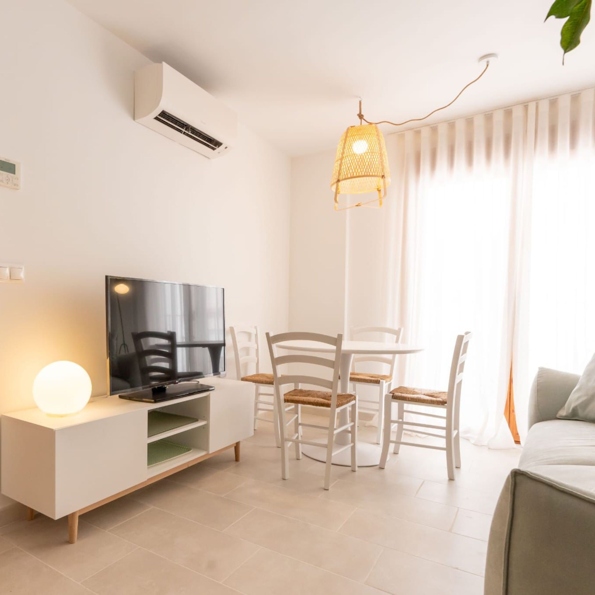 Un salon moderne doté d’un téléviseur à écran plat, d’un meuble de rangement blanc, d’une table à manger avec des chaises et d’un luminaire suspendu.