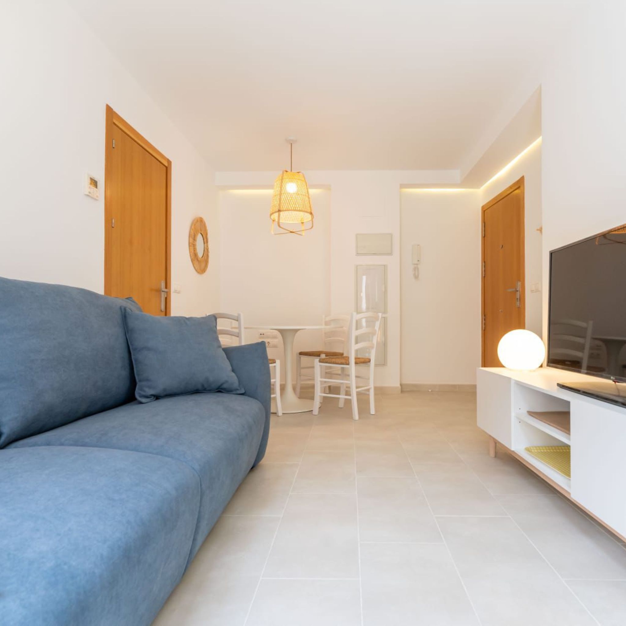 Een moderne woonkamer met een bank, een eettafel met stoelen, een televisie op een standaard en een hanglamp.