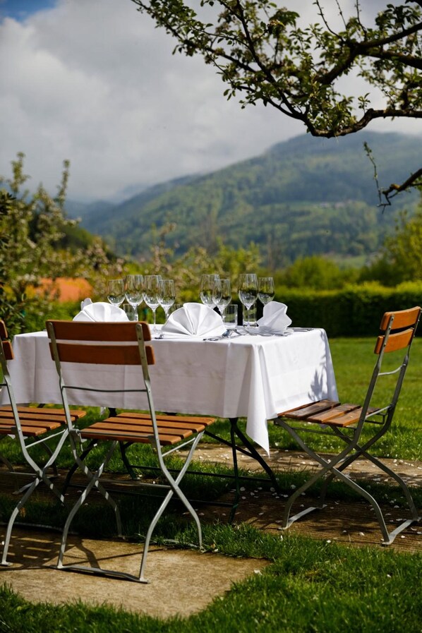 Un espace de restauration en plein air avec une table dressée pour quatre personnes, entourée de chaises, dans un paysage verdoyant luxuriant avec des montagnes en arrière-plan.