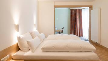 Ein Hotelzimmer mit Bett, Stuhl, Tisch und Blick ins Freie.
