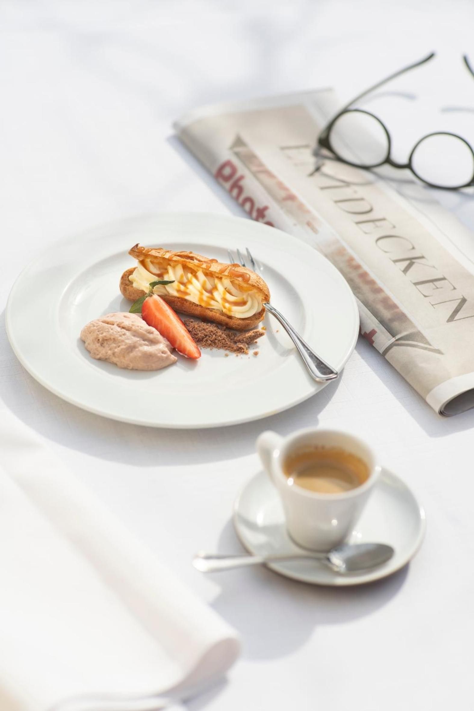 Ein Teller mit Dessert, einer Karotte und einem Löffel auf einem Tisch mit einer Zeitung und Gläsern.
