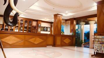 Zona de recepción con mostrador de madera, techo decorativo grande y puerta de vidrio que da al exterior.