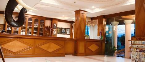 A reception area with a wooden reception desk, a large decorative ceiling, and a glass door leading outside.