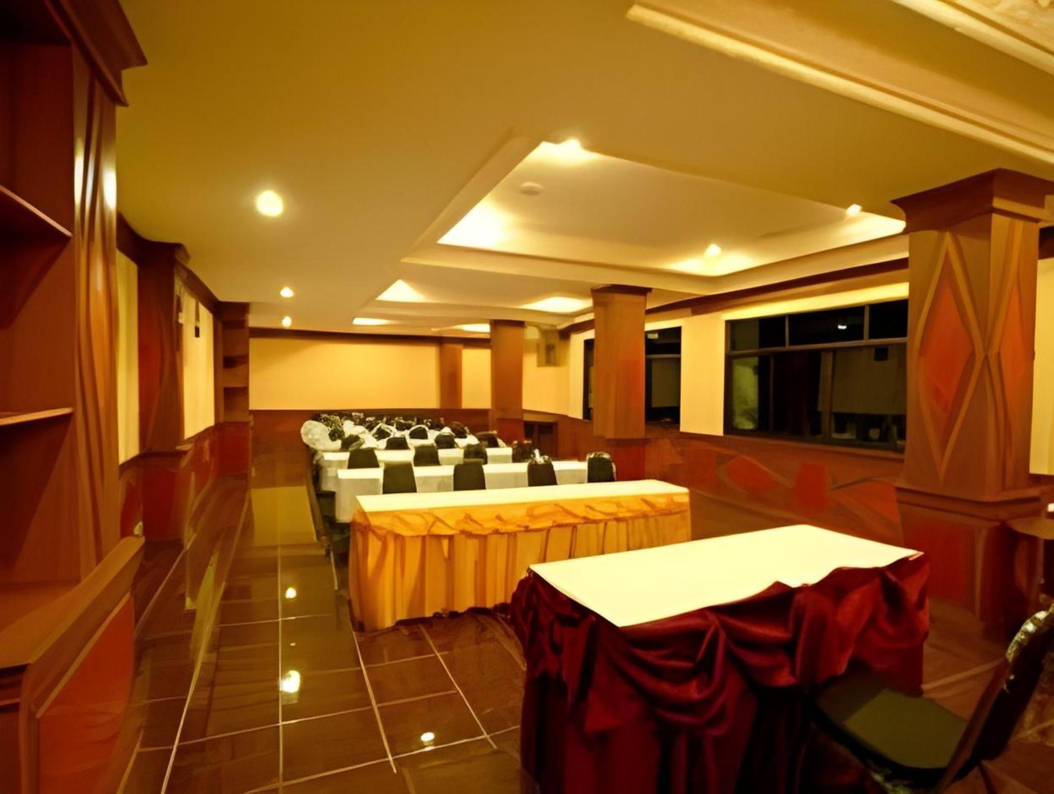 Un salón de conferencias con filas de mesas, un escenario y un ventanal grande.