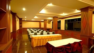 Un salón de conferencias con filas de mesas, un escenario y un ventanal grande.