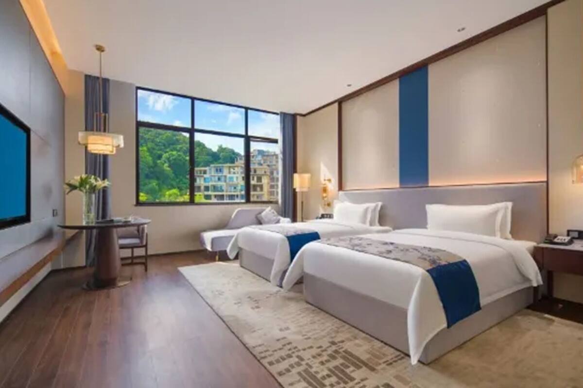 Habitación de hotel moderna con una cama grande, un escritorio y un ventanal con vista a la ciudad.
