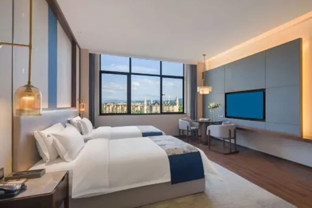A hotel room with a large bed, a desk, a chair, a TV, and a view of the city.