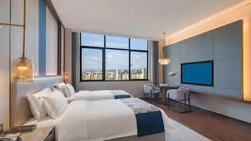 A hotel room with a large bed, a desk, a chair, a TV, and a view of the city.