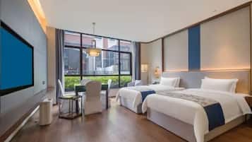 A hotel room with two beds, a desk, and a large window.