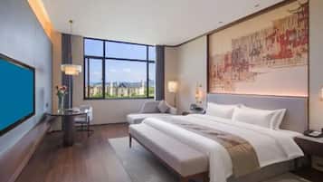 Habitación de hotel con una cama grande, un escritorio, una silla, vistas a la ciudad y una obra de arte de gran tamaño en la pared.