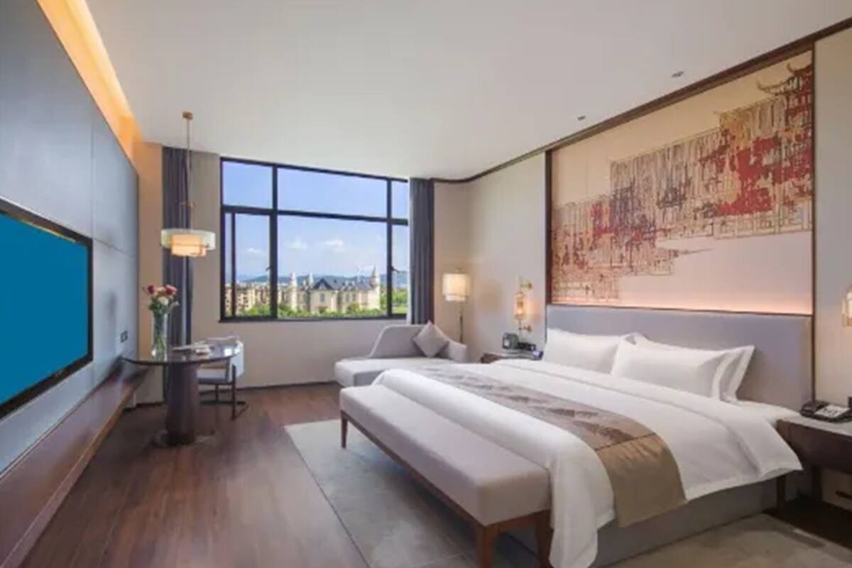 Habitación de hotel con una cama grande, un escritorio, una silla, vistas a la ciudad y una obra de arte de gran tamaño en la pared.
