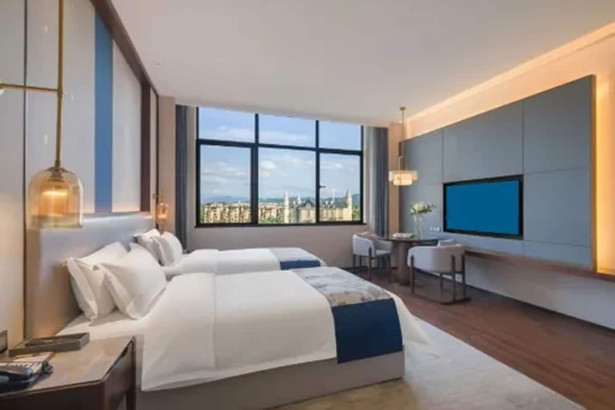 Habitación de hotel con una cama grande, un escritorio, una silla, un televisor y vistas de la ciudad.