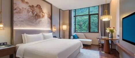 A modern hotel room with a large bed, a seating area, a TV, and a painting on the wall.