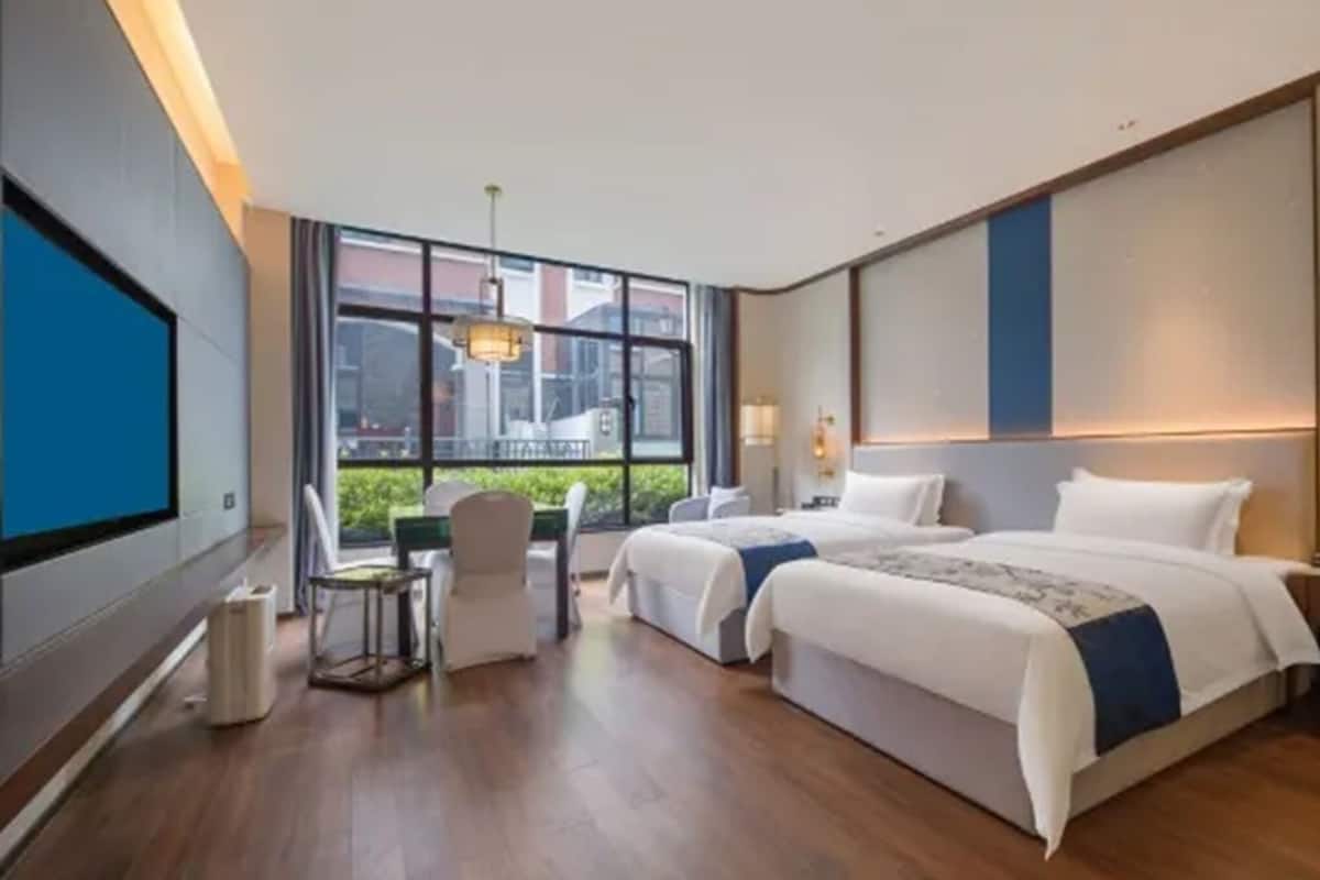 Una habitación de hotel con dos camas, un escritorio y un ventanal amplio.