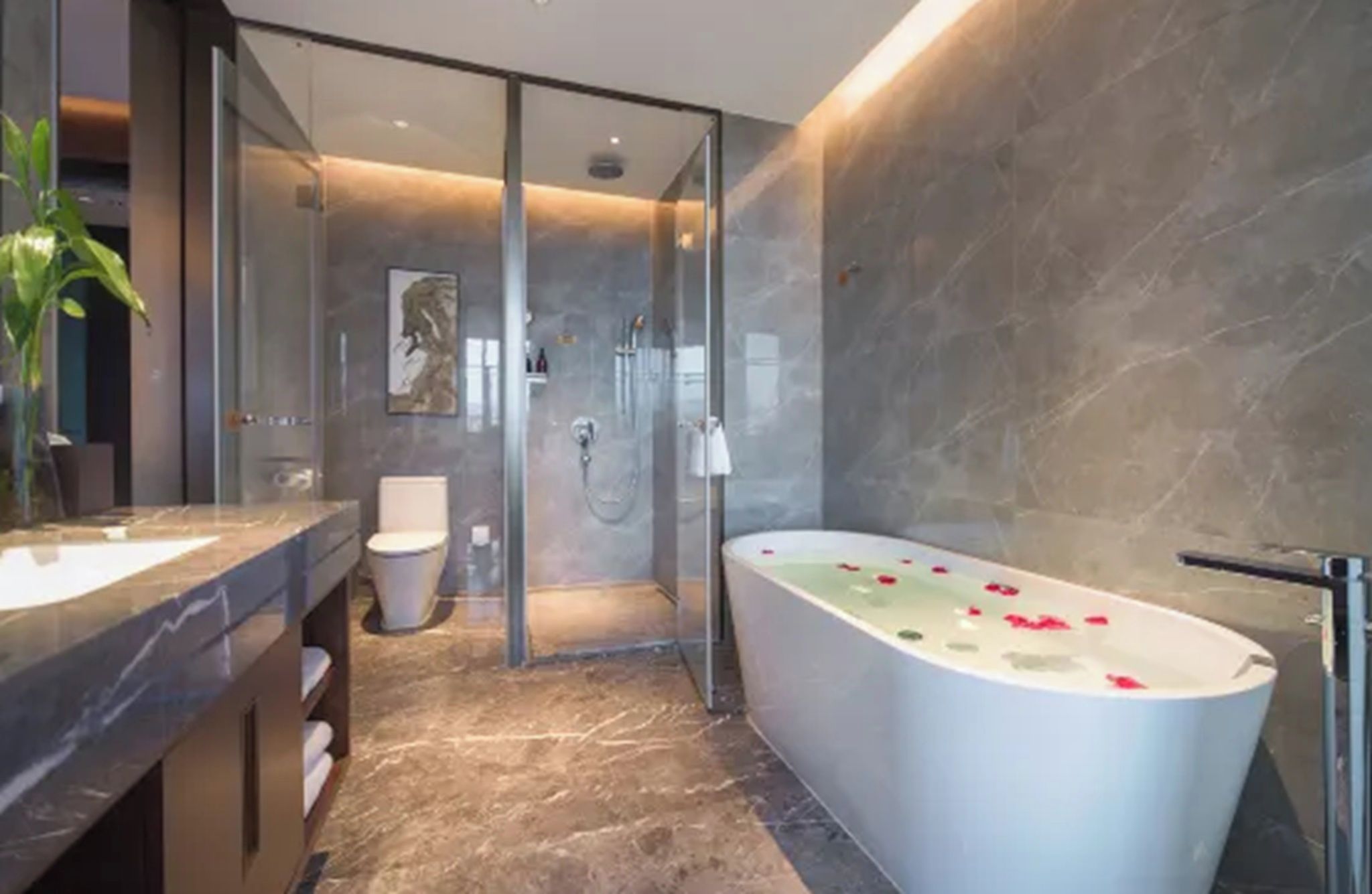 A modern bathroom with a glass shower enclosure, a freestanding bathtub, and a marble floor.