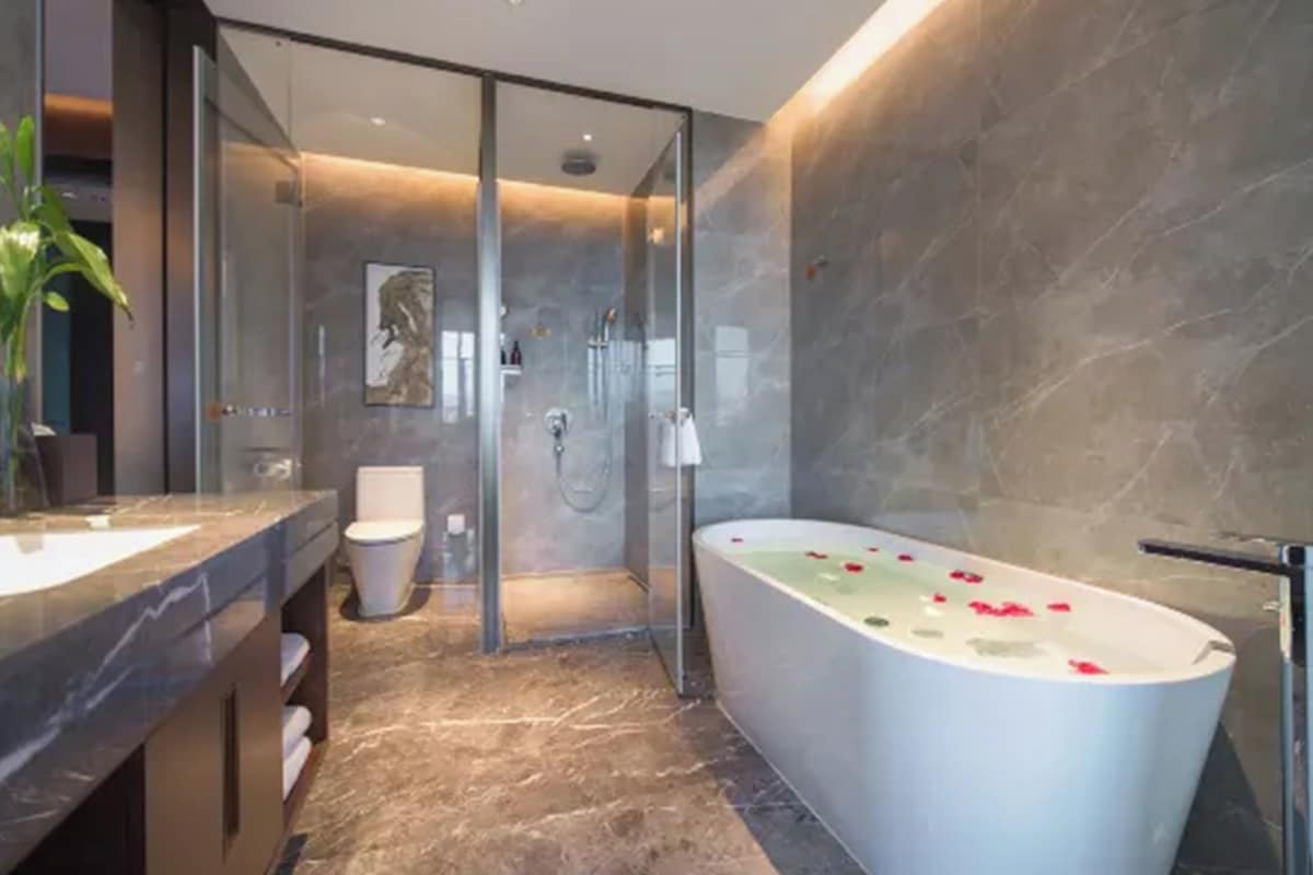 A modern bathroom with a glass shower enclosure, a freestanding bathtub, and a marble floor.