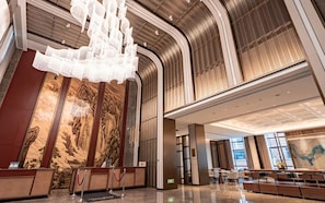 A modern lobby with a reception desk, a chandelier, and a mural on the wall.