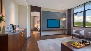 Una sala de estar moderna con un televisor de pantalla plana montado en la pared, un comedor con una mesa de centro y vistas al exterior a través de amplios ventanales.