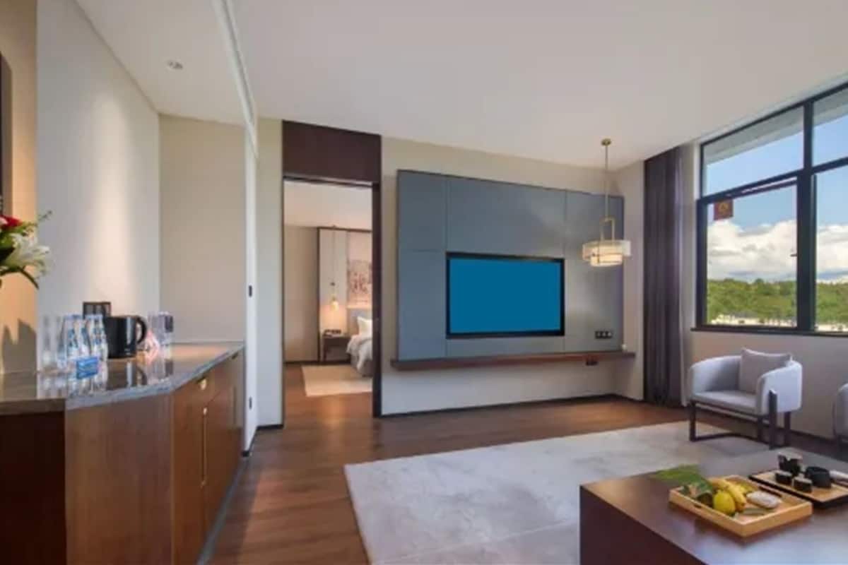 Una sala de estar moderna con un televisor de pantalla plana montado en la pared, un comedor con una mesa de centro y vistas al exterior a través de amplios ventanales.