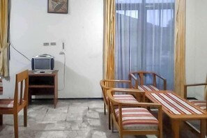 A room with a television on a stand, a table with chairs, and a window with curtains. - Mataram Cottage Syariah Redpartner (Cipanas)