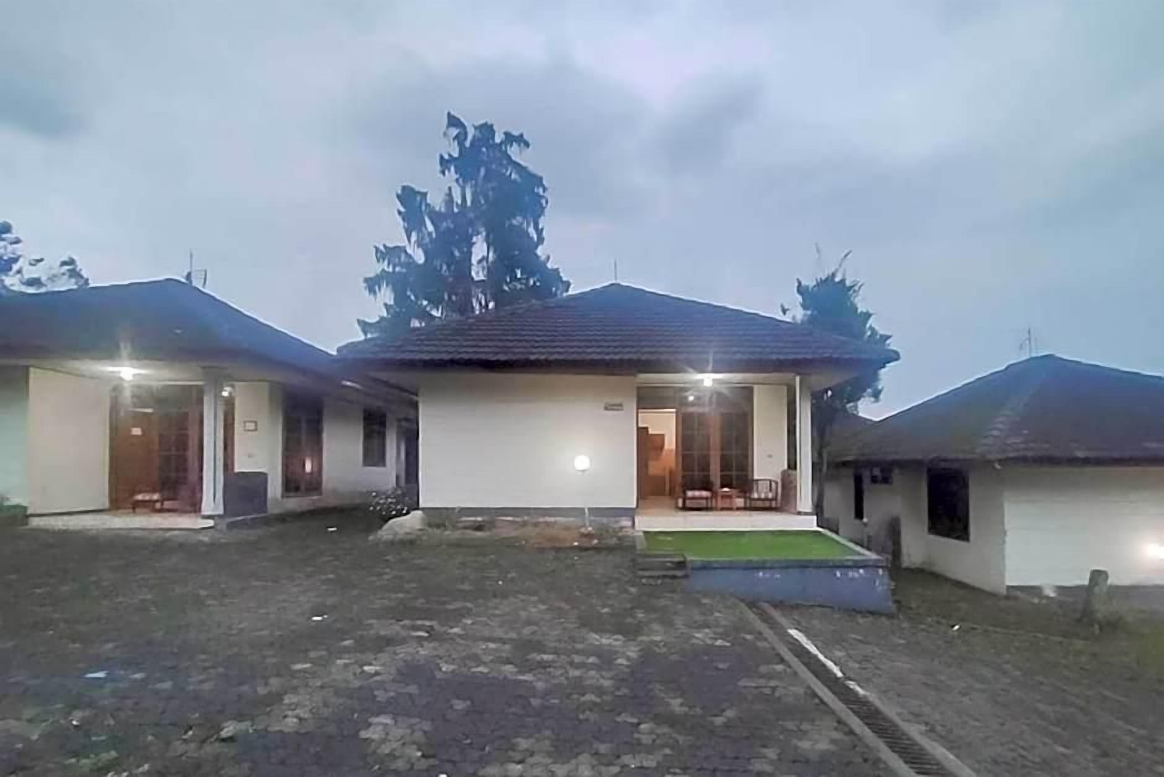 Un edificio a due piani con tetto piatto, un portico anteriore e un piccolo giardino piantumato con una zona pavimentata.