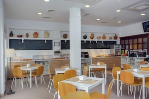 A modern restaurant interior with white tables, orange chairs, and a chalkboard menu.
