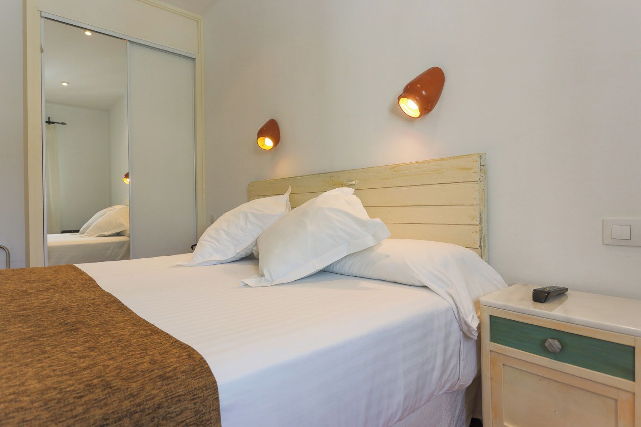 A hotel room with a bed, bedside table, and a mirror.
