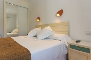 A hotel room with a bed, bedside table, and a mirror.