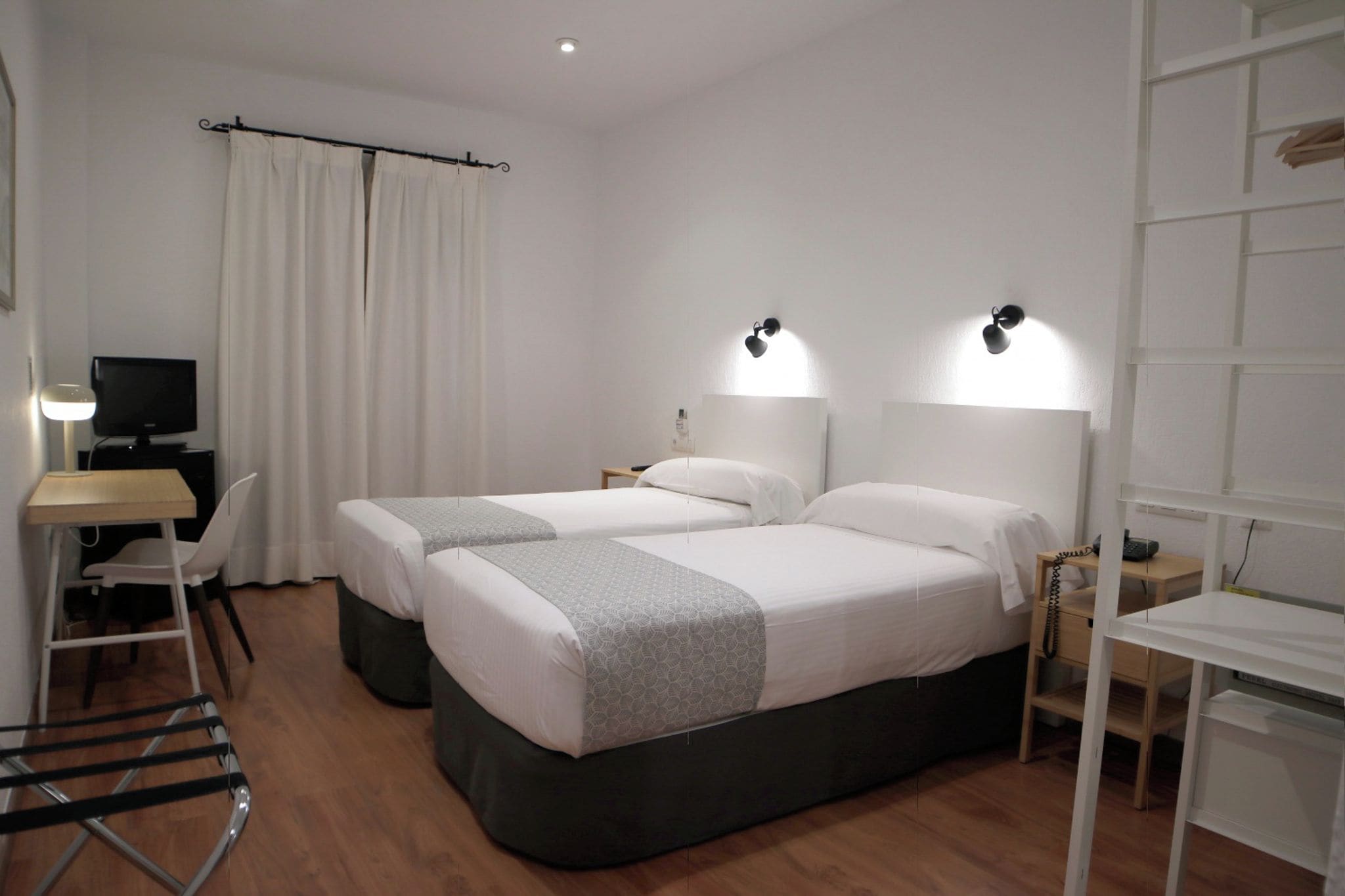 Une chambre d’hôtel avec deux lits, un bureau, une chaise, une télévision et une petite table.