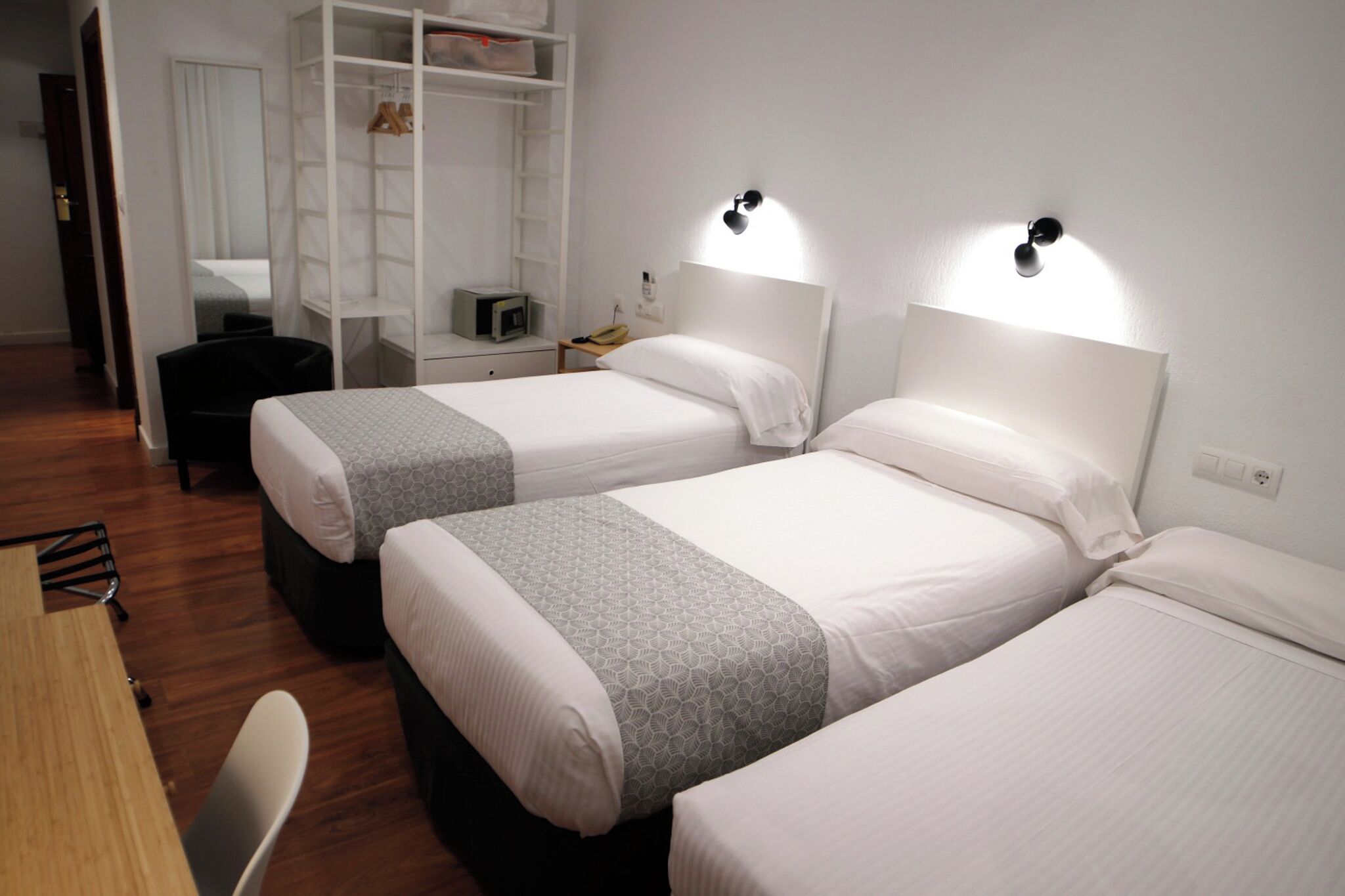 A hotel room with two beds, a desk, a chair, a wardrobe, and a mirror.