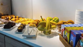 Un bufé con distintos tipos de alimentos, incluyendo pasteles, frutas y cajas de cereales.