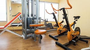 Academia com equipamentos de exercício, um relógio na parede e uma janela.