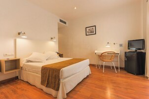 A hotel room with a bed, a desk, a chair, a television, and a small cabinet.
