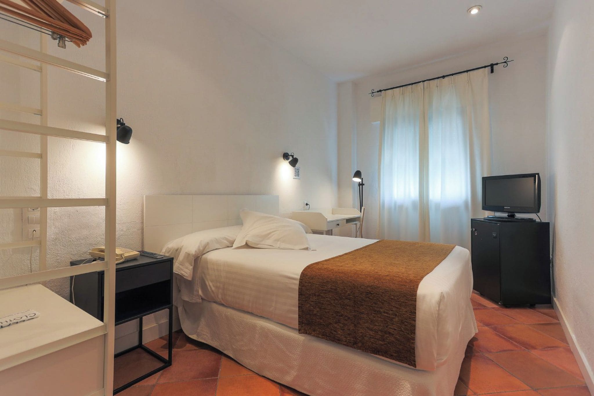 A hotel room with a bed, a desk, a television, and a window with curtains.