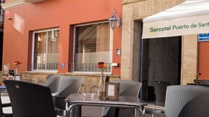 Uma área externa com assentos de metal, cadeiras e mesas, um poste de luz e um edifício com uma placa indicando 'Sercotel Puerto de Sant'.