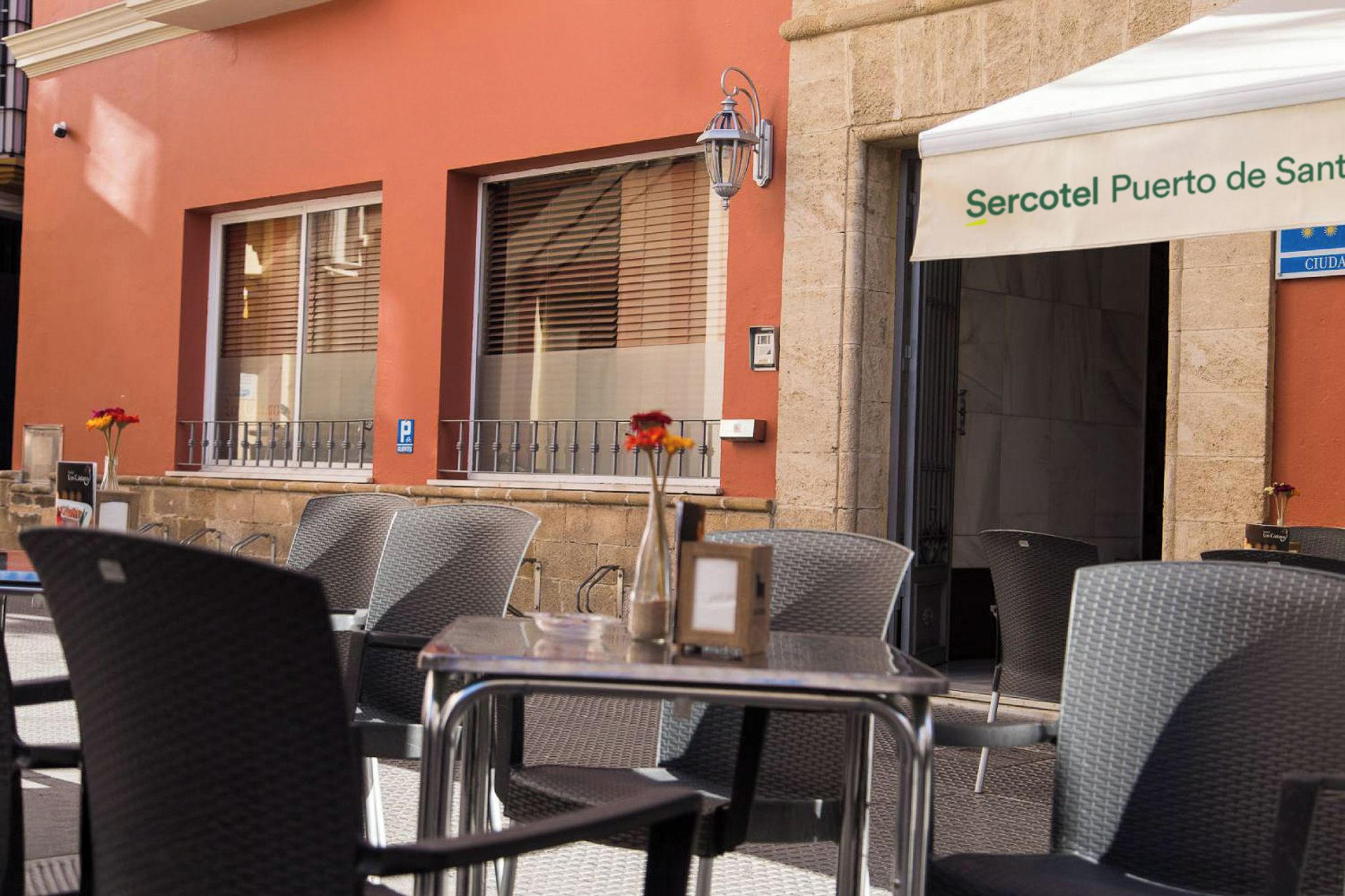 An outdoor seating area with metal chairs and tables, a street lamp, and a building with a sign reading 'Sercotel Puerto de Sant.'