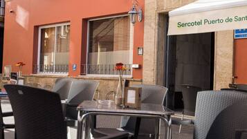 An outdoor seating area with metal chairs and tables, a street lamp, and a building with a sign reading 'Sercotel Puerto de Sant.'