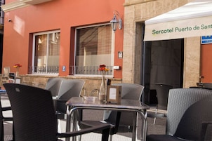 An outdoor seating area with metal chairs and tables, a street lamp, and a building with a sign reading 'Sercotel Puerto de Sant.'