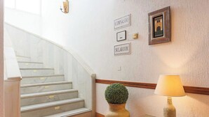 Escada com acabamento em mármore, luminária na parede, quadro emoldurado e planta em vaso.