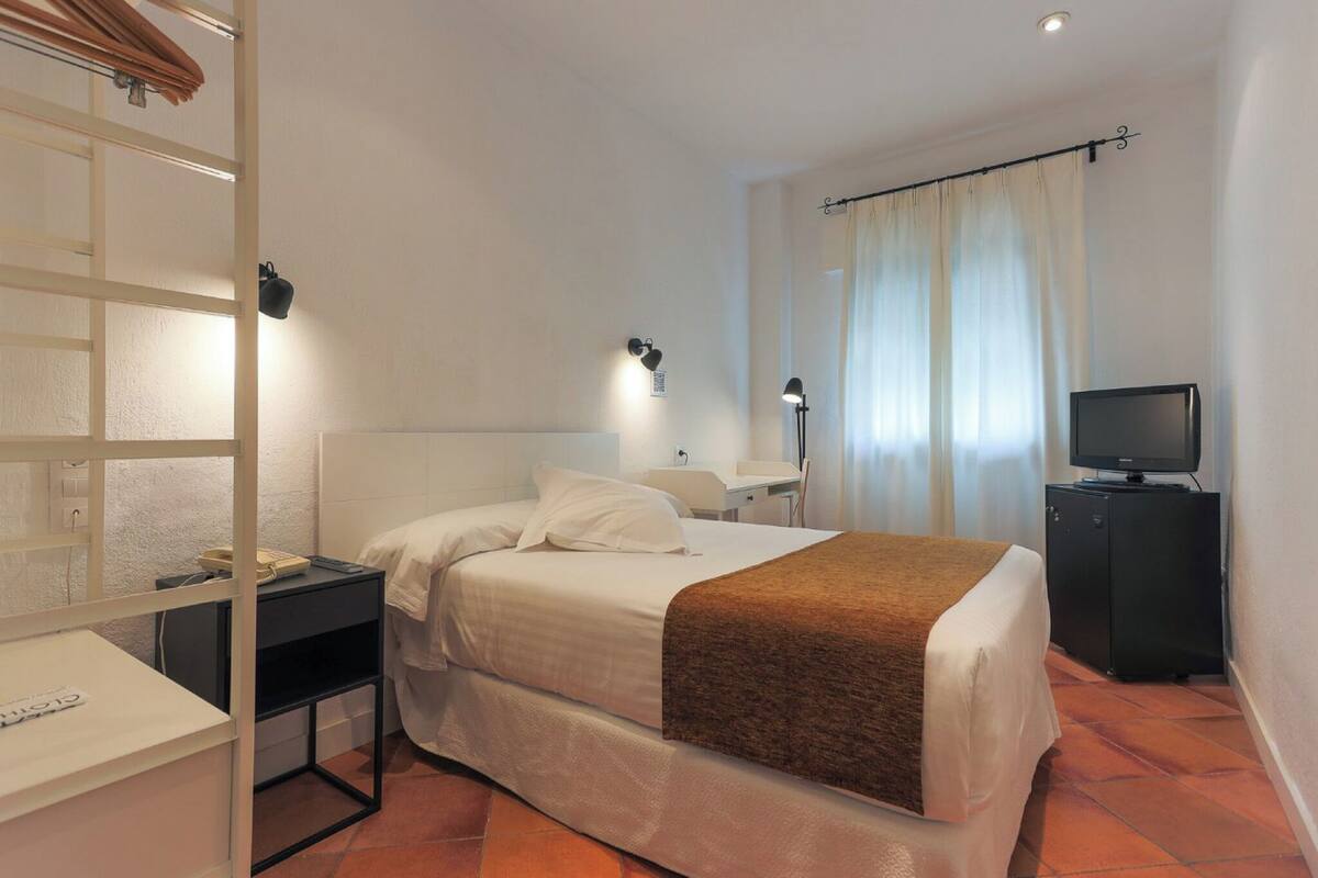 A hotel room with a bed, a desk, a television, and a window with curtains.