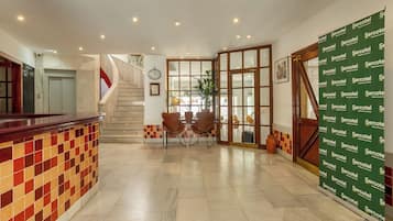 A hotel lobby with a reception desk, a staircase, and a seating area with chairs.