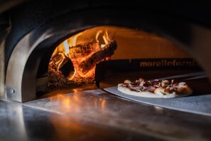 A pizza inside a wood-fired oven with visible flames. - Hammeum Hotel (Prokuplje)