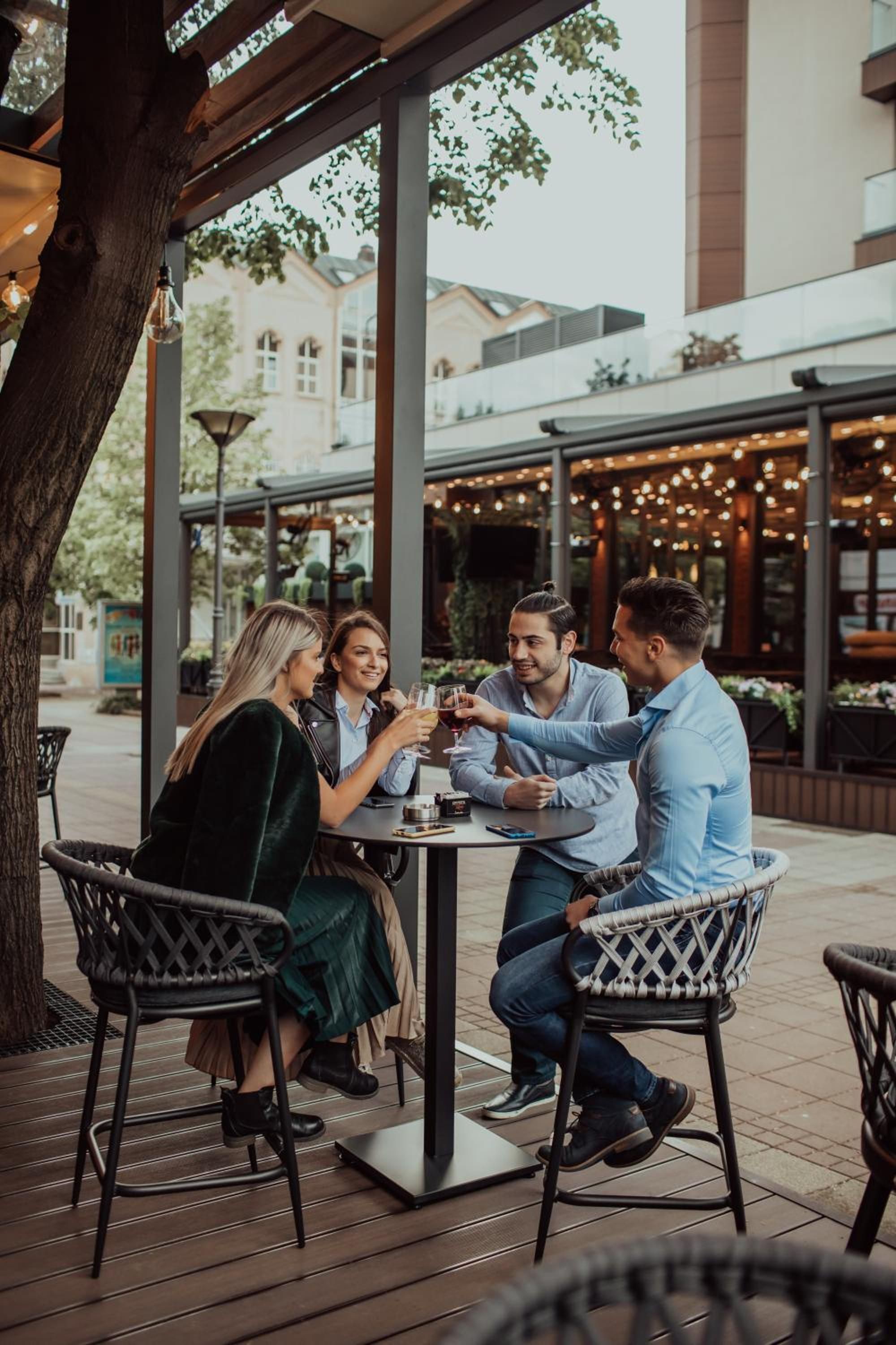 A group of people seated at an outdoor table with a view of a building in the background.