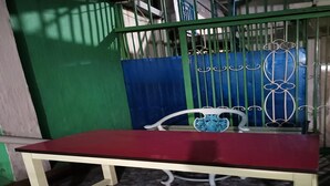 Una mesa roja con estructura blanca, ubicada frente a una reja metálica con detalles decorativos.