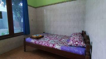 A single bed with a patterned bedspread, a window with blue curtains, and a tiled floor.