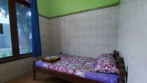 Una cama individual con una colcha estampada, una ventana con cortinas azules y un suelo de baldosas.