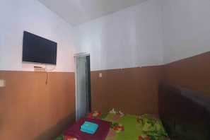 Una habitación pequeña con una cama, un televisor colgado en la pared y una puerta.